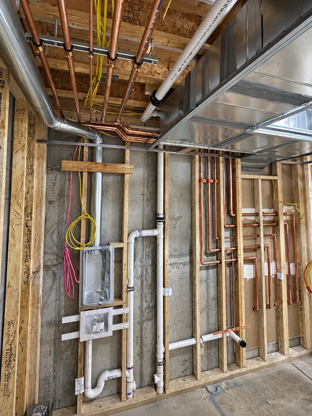 Plumbing rough-in with copper and PVC lines in framed wall
